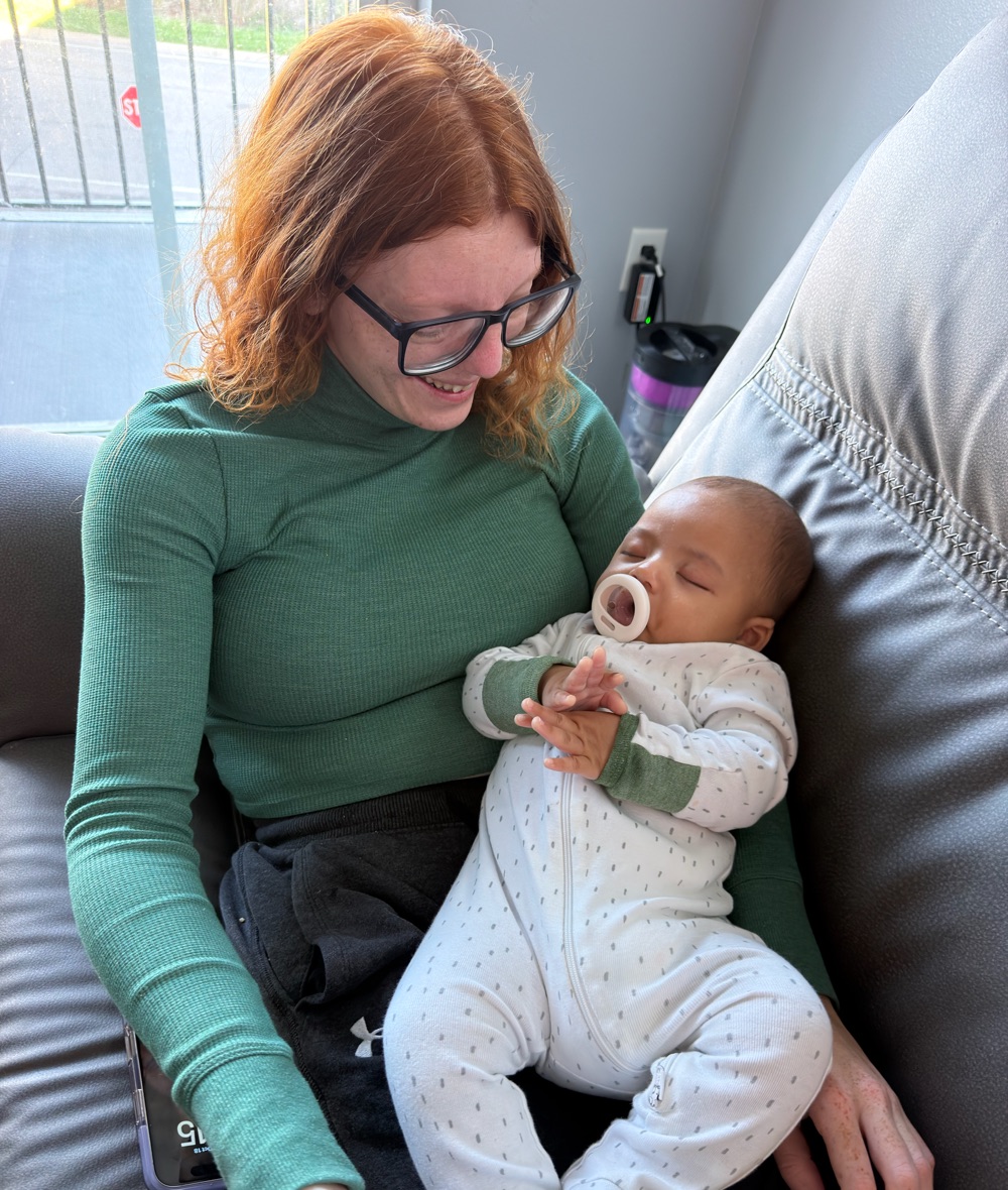 Brandy smiling down at a sleeping baby on her lap